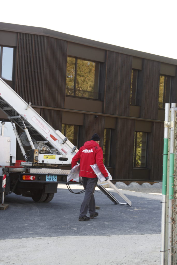 Un déménageur porte 2 ordinateurs devant le nouveau bâtiment.